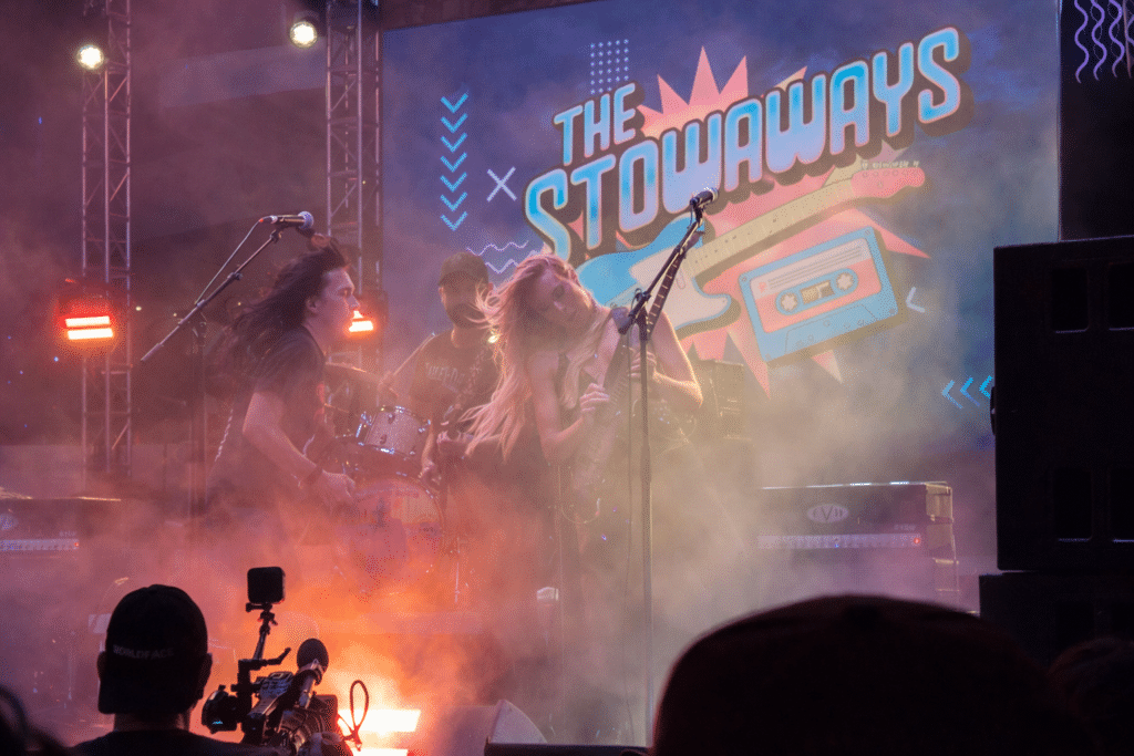 The Stowaways performing live on the ShipRocked 2025 main deck stage at night with smoke, lighting, and crowd silhouettes