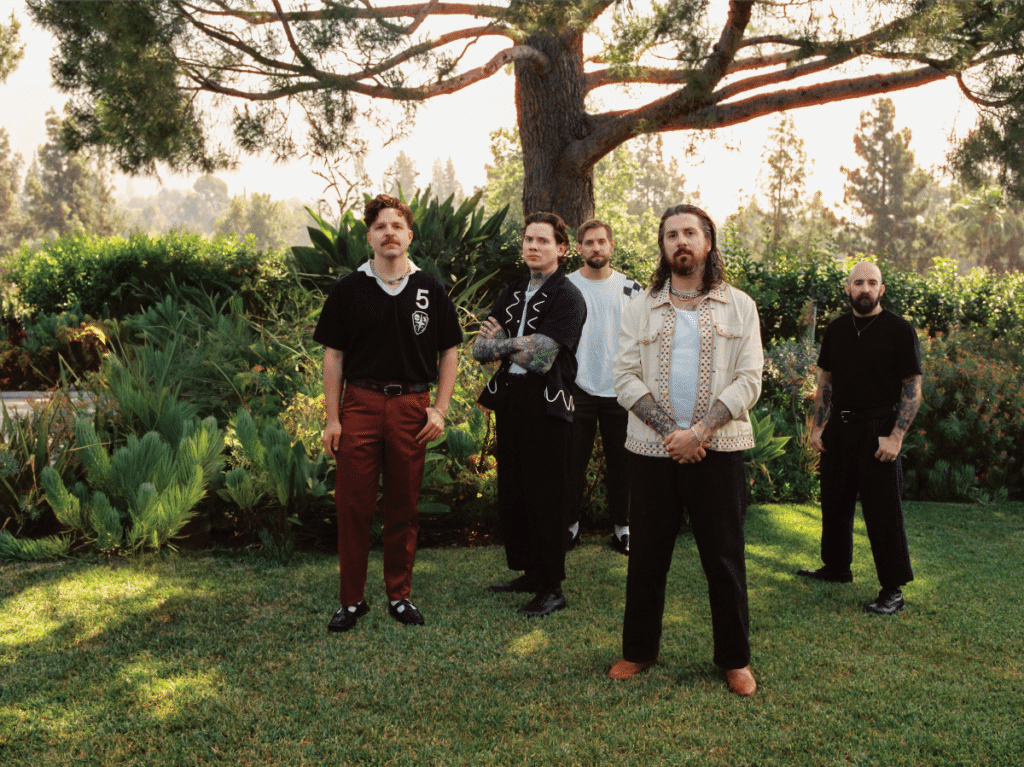The Devil Wears Prada band members standing outdoors in a lush garden setting, wearing casual and modern outfits during their Flowers era.